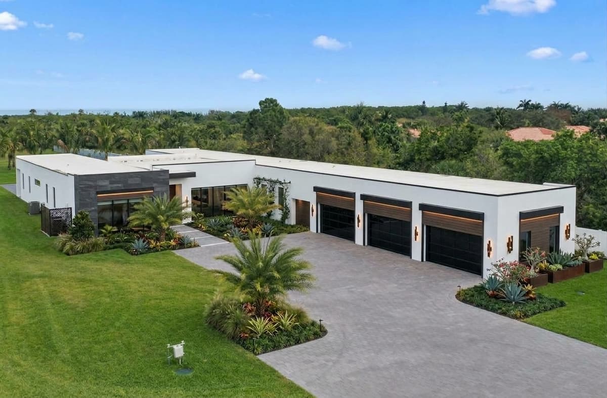 A villa at The Palms: a long single-story modern residence in white stucco with dark stone and wood accents, a three-car garage and tropical landscaping