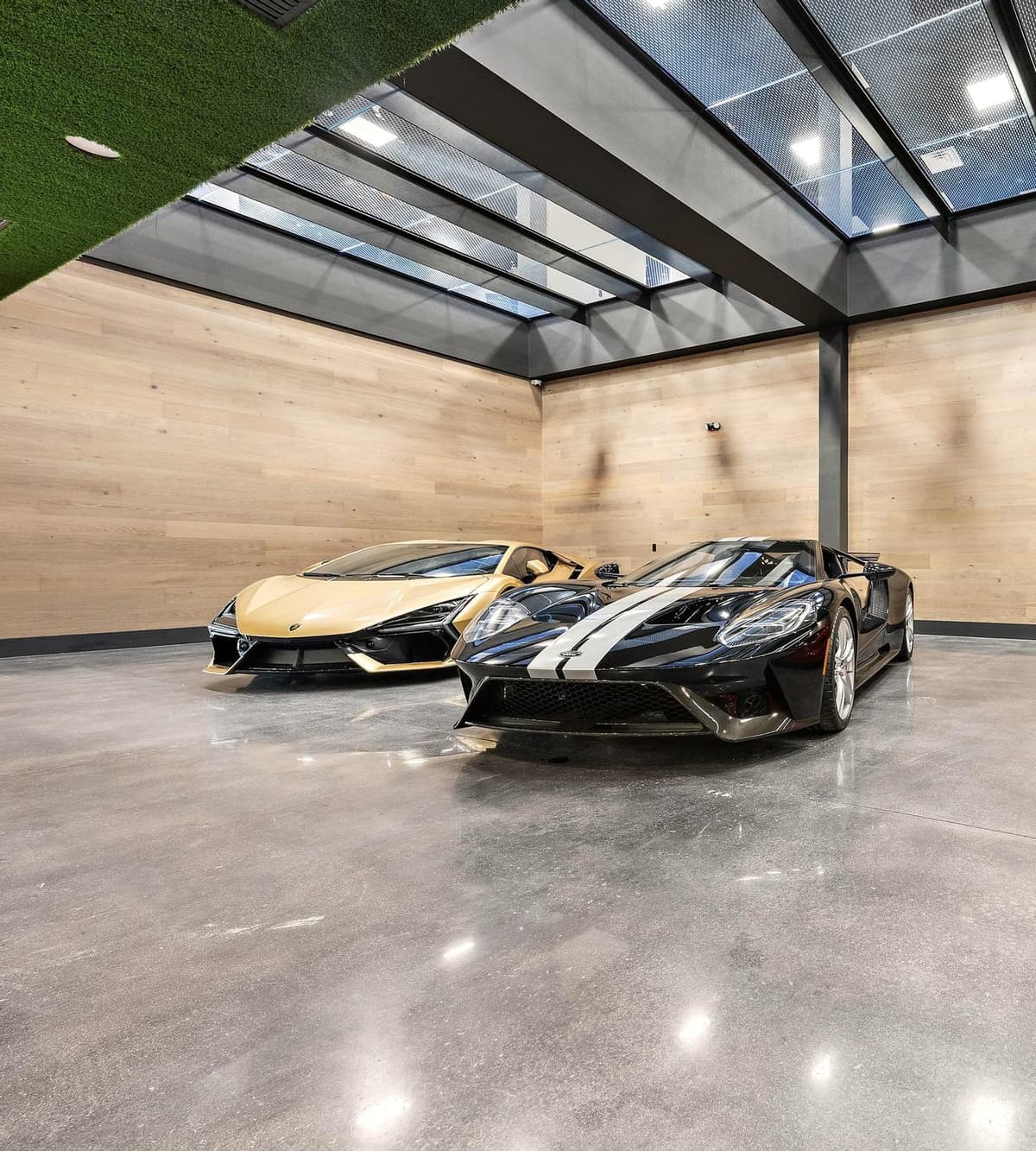 Ground-floor gallery of polished concrete and pale timber under the glass floor, two cars parked side by side