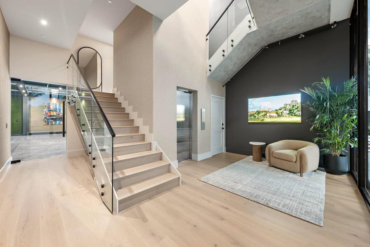Timber stair with a glass balustrade rising from a reception area with an armchair and a potted palm