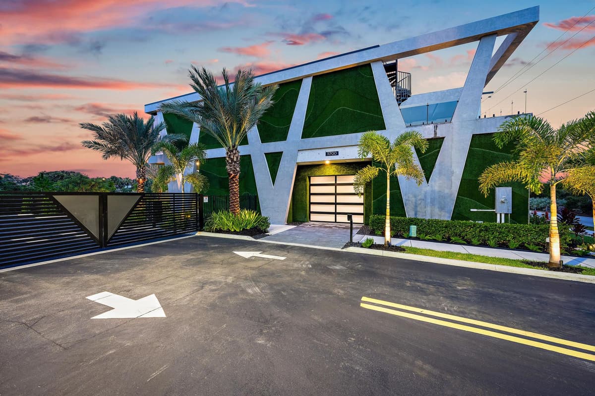 The Bunker in Hobe Sound at dusk: white V-shaped columns framing planted green walls and a glass garage door, palms along a gated drive